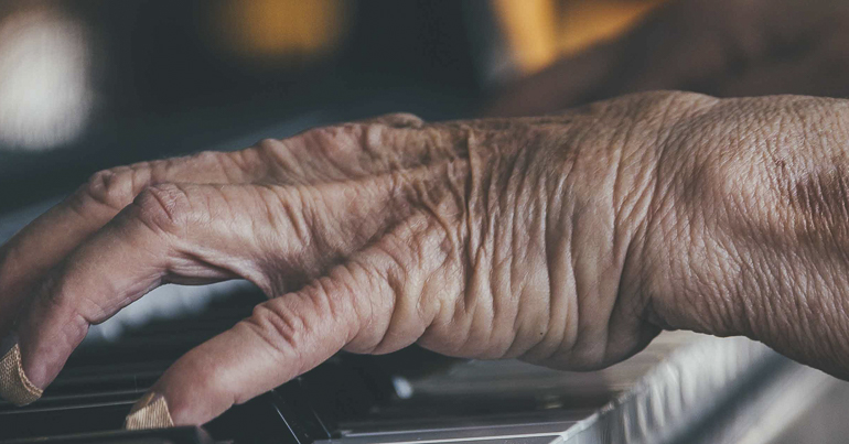 aged hand playing a piano