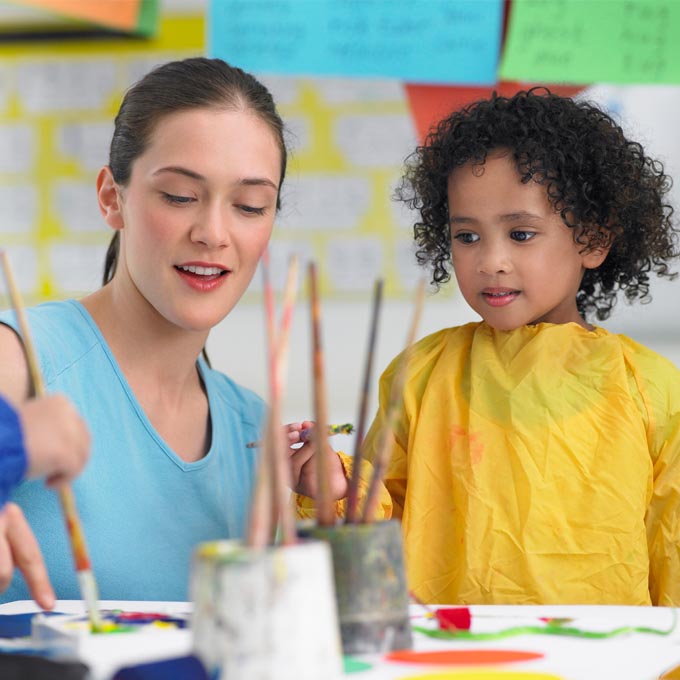 young female teacher with little girl and paint brushes