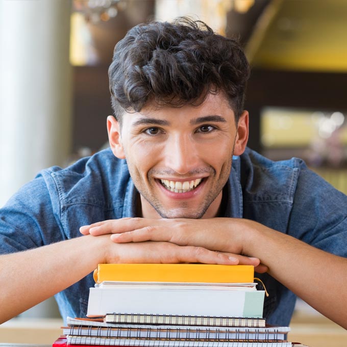 young male smiling with hands over books and spirals