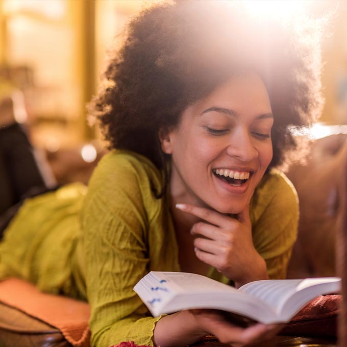 young woman laying on stomach while reading a book and smiling